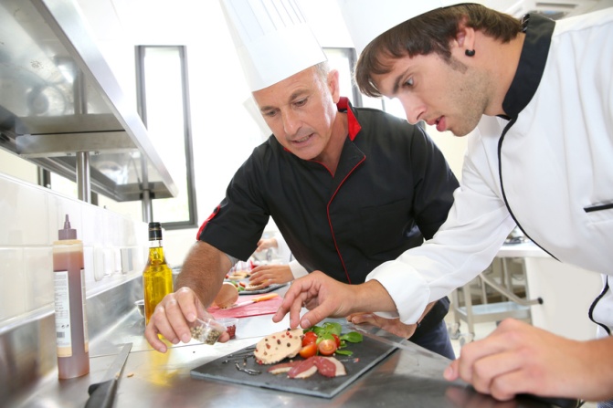 Chef helping student in catering to prepare foie gras dish