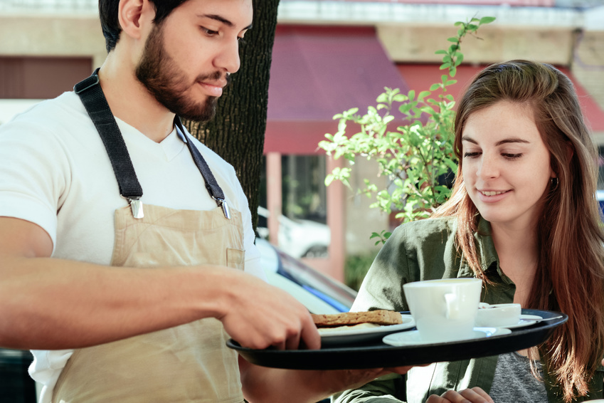 Young waiter serving coffee to female customer